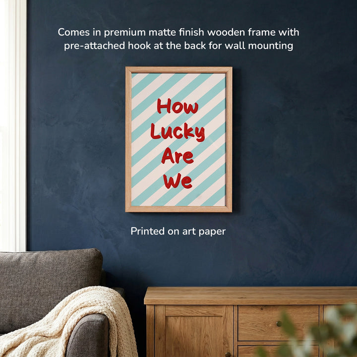 How Lucky Are We Frame mounted on the blue wall, with the text that it has pre-attached hooks for the mounting, premium matte-finish wooden frame 