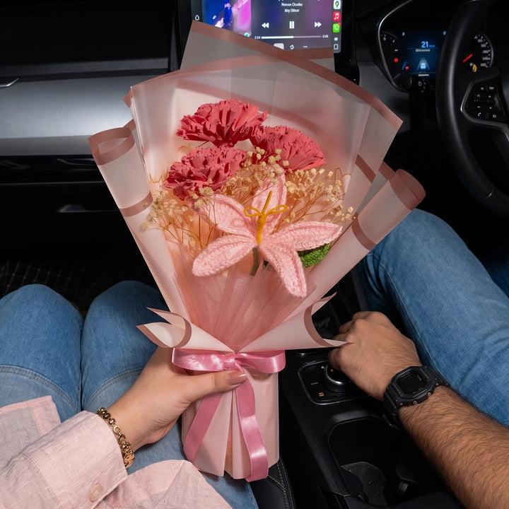 Bouquet of pink flowers with a pink ribbon held by two people inside a car.