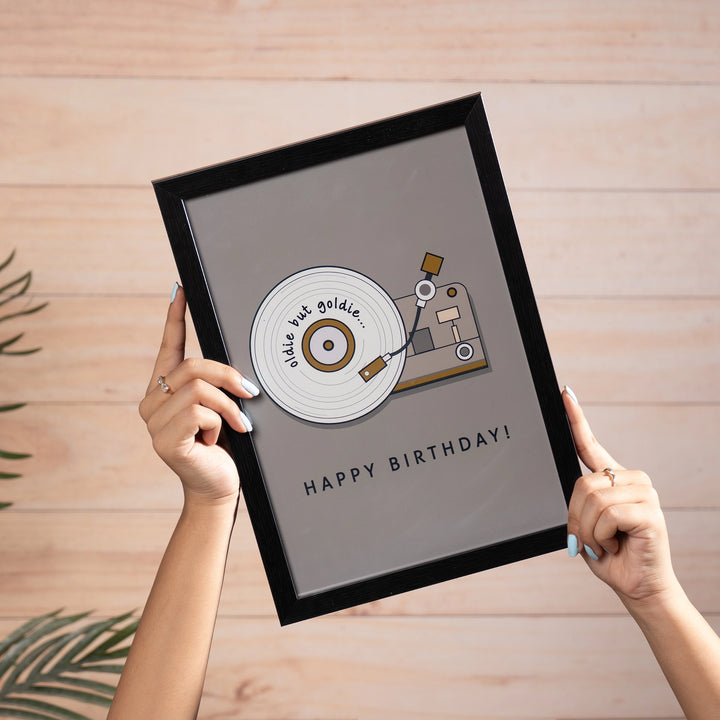 The Retro Spin wall art - the print features an illustrated vinyl record player on a warm grey background with the text "oldie but goldie" written along the record and "Happy Birthday!" in bold lettering below.